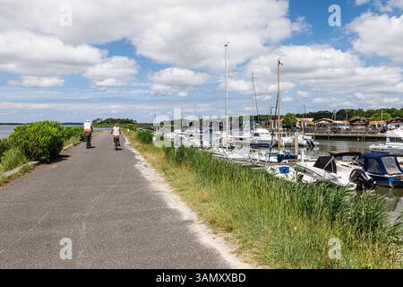 Andernos-les-bains (sud-ouest de la France) : touristes à vélo sur une route le long de la digue entre le bassin d'Arcachon, le port des huîtres et le port de plaisance. CYCL Banque D'Images