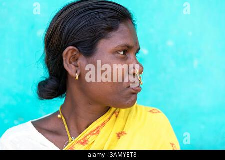 Portrait d'une femme décorée d'anneaux de nez et de bijoux debout devant un mur de boue coloré en Orissa, Inde Banque D'Images
