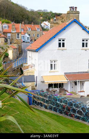 12 avril 2025 Runswick Bay, Royaume-Uni - le pittoresque villabe de Runswick Bay dans le Yorkshire du Nord avec des maisons de villige et des pots de filets à homard empilés. Banque D'Images