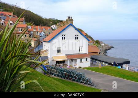 12 avril 2025 Runswick Bay, Royaume-Uni - le pittoresque villabe de Runswick Bay dans le Yorkshire du Nord avec des maisons de villige et des pots de filets à homard empilés. Banque D'Images