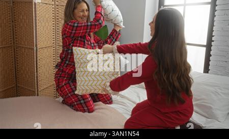 Mère et fille s'amusant avec un combat d'oreiller sur le lit, à l'intérieur, exprimant l'amour de la famille et jouissant joyeusement du temps de qualité ensemble à la maison. Banque D'Images