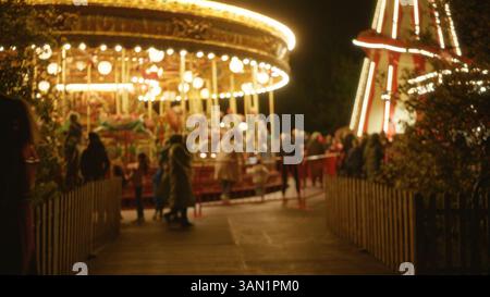 Scène de nuit avec des gens flous profitant du carrousel festif dans un parc, avec des lumières vives, des effets de bokeh, et divers hommes et femmes créant un jofu Banque D'Images