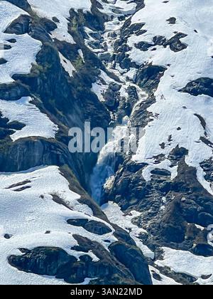 Une superbe cascade coule à travers un col de montagne accidenté, coupant à travers la neige et la glace. La puissance et la beauté de la nature en plein écran dans un WO alpin Banque D'Images
