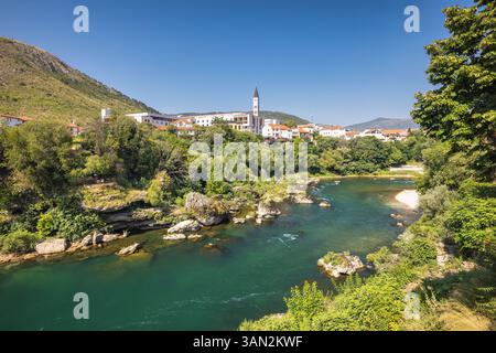 Rivière Neretva dans la ville de Mostar, Bosnie-Herzégovine, Europe. La rivière coule à travers une ville européenne. Une végétation luxuriante entoure les bâtiments avec des montagnes Banque D'Images