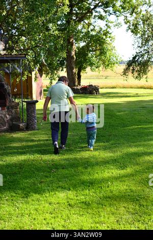 Grand-mère et petit-fils allant ensemble se tenant la main dans la campagne dans la zone rurale ensoleillée de jour d'été. Petit-enfant et grand-mère passant du temps ensemble. TW Banque D'Images