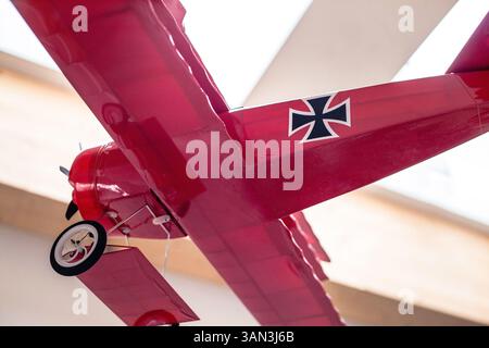 Petit avion baron rouge suspendu comme décoration sur fond blanc. Vue de bas, montrant une croix rouge typique. Banque D'Images