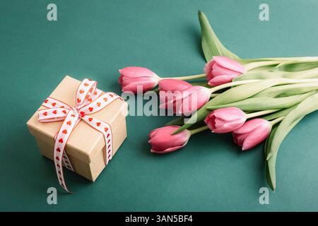 Boîte cadeau avec ruban rouge et bouquet de tulipes roses sur fond vert. Concept de vacances de printemps. Vue de dessus. Banque D'Images