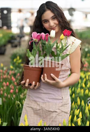 Joyeuse fille tient des tulipes rouges jaunes dans le pot contre une floraison de tulipes. L'enfant heureux tient des pots de fleurs de jardin. Printemps, jardinage et Pâques Concepp Banque D'Images