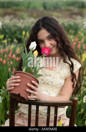 fille tenir des tulipes rouges jaunes dans le pot contre une tulipe floue. L'enfant heureux tient un pot de fleurs de jardin. Printemps, jardinage et concept de Pâques Banque D'Images