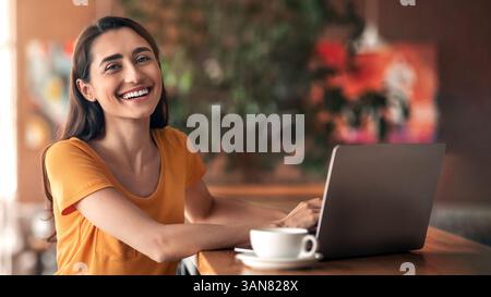 Une dame arabe joyeuse assise devant un ordinateur portable au café Banque D'Images