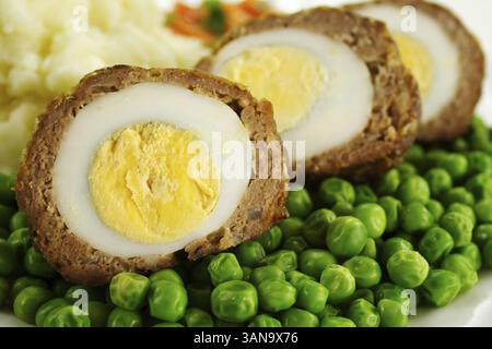 Délicieux œufs de scotch avec petits pois, carottes et purée de pommes de terre Banque D'Images