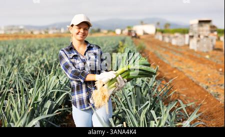Horticulteur féminin réussi avec des poireaux dans les mains debout sur le terrain Banque D'Images