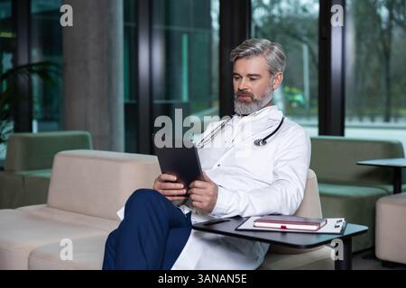 Médecin masculin mature aux cheveux gris travaillant et paraissant occupé Banque D'Images