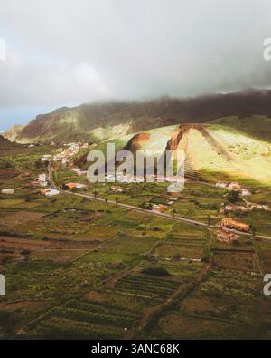 Vue aérienne des montagnes verdoyantes et des champs pittoresques avec un village tranquille sous un ciel nuageux, Buenavista del Norte, Espagne. Banque D'Images
