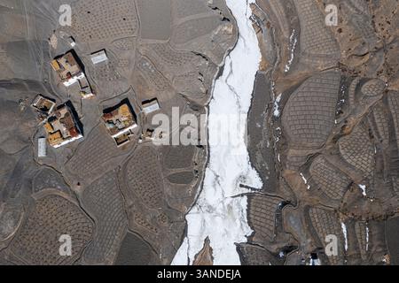 Vue aérienne d'une petite colonie de maisons le long d'un ruisseau gelé avec quelques champs agricoles près de Kaza township, Himachal Pradesh, Inde. Banque D'Images