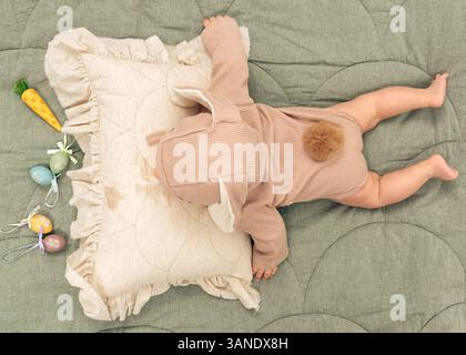 Un charmant bébé portant un costume de lapin moelleux explore une aire de jeux douce, câlin avec des lapins en peluche dans un environnement chaleureux et serein. Banque D'Images