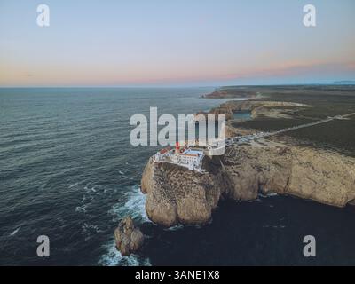 Vue aérienne du majestueux phare de Farol do Cabo de Sao Vicente sur une falaise accidentée surplombant l'océan serein au coucher du soleil, Sagres, Portugal. Banque D'Images