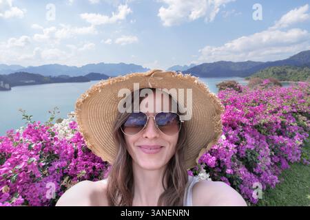 Portrait d'une voyageuse en lunettes de soleil et un chapeau de paille prenant des selfies dans le contexte de la nature thaïlandaise, le lac Cheo LAN dans le parc Khao Sok. Banque D'Images