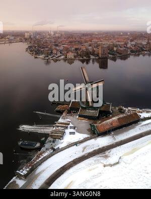 Vue aérienne d'une scène hivernale pittoresque avec des moulins à vent enneigés et une rivière tranquille, Zaanse Schans, pays-Bas. Banque D'Images