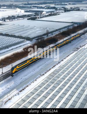Vue aérienne de serres enneigées et d'un train sur une voie ferrée, Heerhugowaard, pays-Bas. Banque D'Images