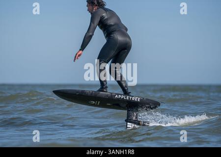 Un homme dans une combinaison noire monte une tranchée hydrofoil électrique foilboard, dans la mer par une journée ensoleillée, efoil, foil drive, foil hybride assistance. Banque D'Images