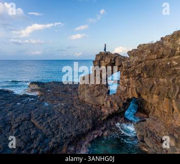 Vue aérienne d'une personne debout seule au sommet d'une arche naturelle le long de la côte, île Maurice. Banque D'Images