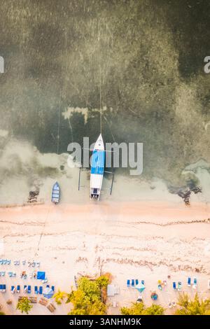 Vue aérienne d'un petit voilier amarré sur la plage de sable doré de Gili Air Island avec parasol et lits de plage, West Nusa Tenggara, Indonésie. Banque D'Images