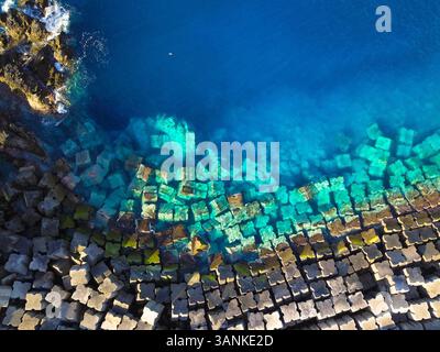 Vue aérienne de belles vagues turquoises de l'océan s'écrasant contre les rochers et les blocs de béton, Porto Moniz, Portugal. Banque D'Images