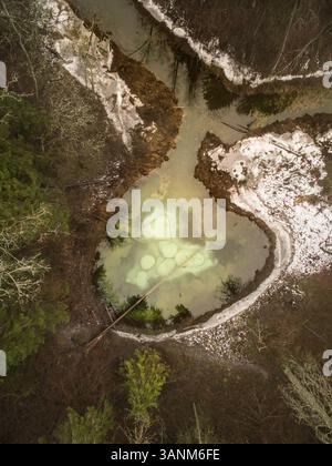Vue aérienne d'un petit lac gelé au milieu de la forêt enneigée en Estonie. Banque D'Images