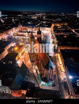 Vue aérienne de la place principale illuminée avec église Marie et Sukiennice dans un paysage urbain animé, Cracovie, Pologne. Banque D'Images