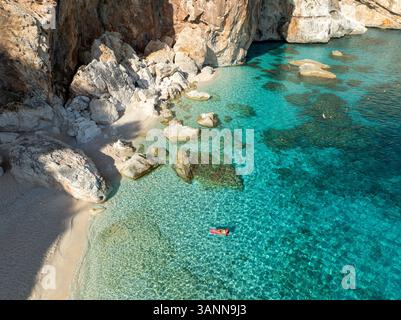 Vue aérienne de la plage de mariolu avec une femme sur un matelas gonflable entouré d'eau turquoise et de falaises rocheuses, Baunei, Italie. Banque D'Images
