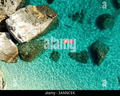 Vue aérienne de la plage de mariolu avec une femme sur un matelas gonflable entouré d'eau turquoise et de côte rocheuse, Baunei, Italie. Banque D'Images