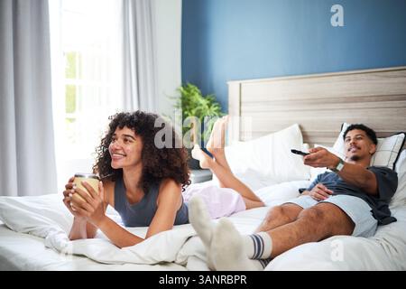 Jeune couple de détente ensemble dans le lit avec café et TV télécommande Banque D'Images