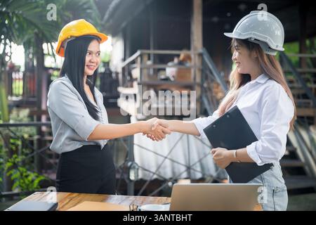 Deux femmes asiatiques architecte et ingénieur en casques de protection se serrant la main après la réunion. Concept de collaboration réussie. Banque D'Images