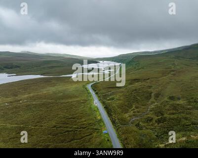 Vue aérienne d'une route sinueuse le long d'une rivière et de montagnes dans les magnifiques Highlands écossais, Portree, Royaume-Uni. Banque D'Images