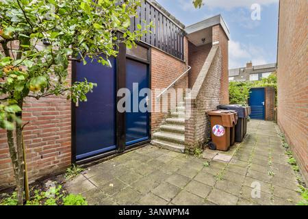 Une ruelle urbaine étroite avec un escalier, des poubelles et de la verdure, offrant un aperçu de la vie urbaine et de l'architecture dans un quartier résidentiel. Banque D'Images