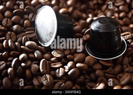 Détail de deux capsules espresso en aluminium noir sur un tas de grains de café torréfiés. Vue surélevée de dessus. Banque D'Images