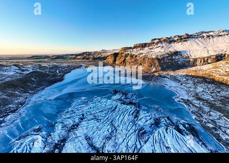 Vue aérienne d'un lac glaciaire serein entouré d'un paysage de montagne majestueux couvert de neige, Skogar, Islande. Banque D'Images