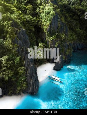 Vue aérienne d'une personne sur une petite plage le long de la côte sauvage avec le littoral et un catamaran amarré à Entalula Island, El Nido, Palawan, Philippines. Banque D'Images
