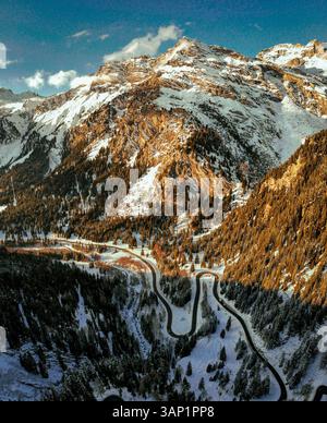 Vue aérienne de la route sinueuse à travers les montagnes enneigées et les vallées luxuriantes, col de Maloja, canton de Graubuenden, Suisse. Banque D'Images