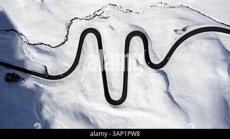 Vue aérienne d'une route sinueuse à travers des montagnes enneigées avec une rivière qui coule, col de Julier, canton de Graubuenden, Suisse. Banque D'Images