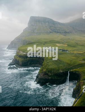 Vue aérienne du village pittoresque de Gasadalur avec une cascade étonnante cascadant d'une falaise accidentée dans l'océan, Vagar, îles Féroé. Banque D'Images