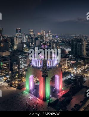 Vue aérienne par drone de Monumento a la Revolucion avec les lumières colorées du drapeau mexicain et l'horizon de la ville à Mexico la nuit, Mexique. Banque D'Images