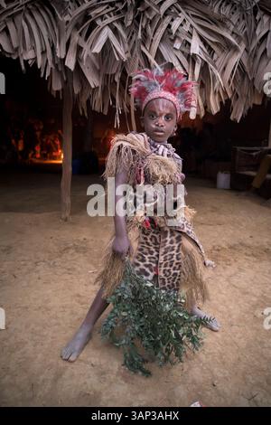 Portrait d'un garçon devant un temple, vêtu d'un costume rituel fait de peaux d'animaux et de plumes, un matin après un Bwiti toute nuit. Banque D'Images