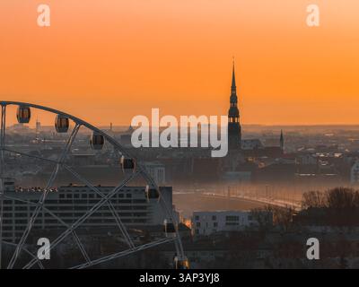 Lever de soleil sur la vieille ville de Riga avec église Pierre et grande roue Banque D'Images