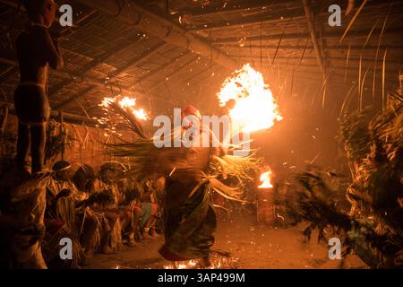 Les participants à une cérémonie des Bwiti, vêtus d'une tenue rituelle faite de feuilles de palmier séchées, dansent avec des torches allumées à l'intérieur d'un petit temple. Banque D'Images
