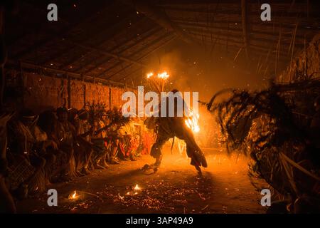 Les participants à une cérémonie des Bwiti, vêtus d'une tenue rituelle faite de feuilles de palmier séchées, dansent avec des torches allumées à l'intérieur d'un petit temple. Banque D'Images