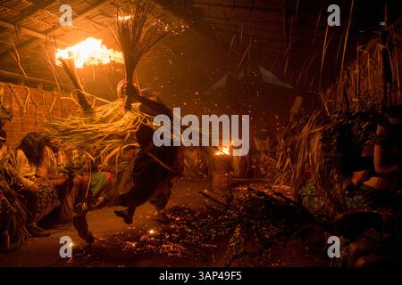 Les participants à une cérémonie des Bwiti, vêtus d'une tenue rituelle faite de feuilles de palmier séchées, dansent avec des torches allumées à l'intérieur d'un petit temple. Banque D'Images