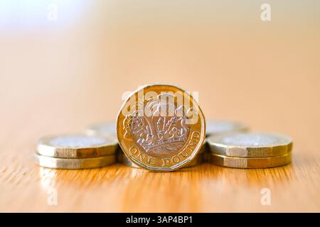 Une seule pièce britannique d'une livre debout sur son bord sur un bureau avec d'autres pièces couchées à plat Banque D'Images
