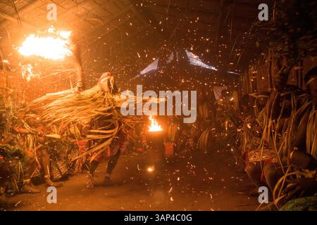 Les participants à une cérémonie des Bwiti, vêtus d'une tenue rituelle faite de feuilles de palmier séchées, dansent avec des torches allumées à l'intérieur d'un petit temple. Banque D'Images